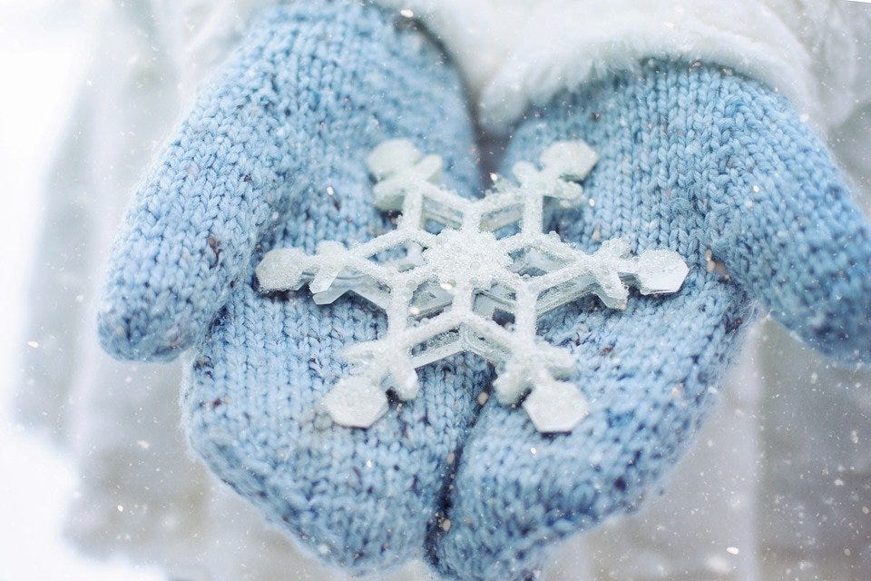 A pair of blue mittens holding a snowflake ornament.