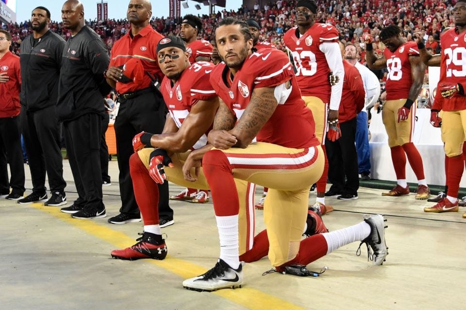 Colin Kaepernick taking a knee with teammates during the national anthem at an NFL match