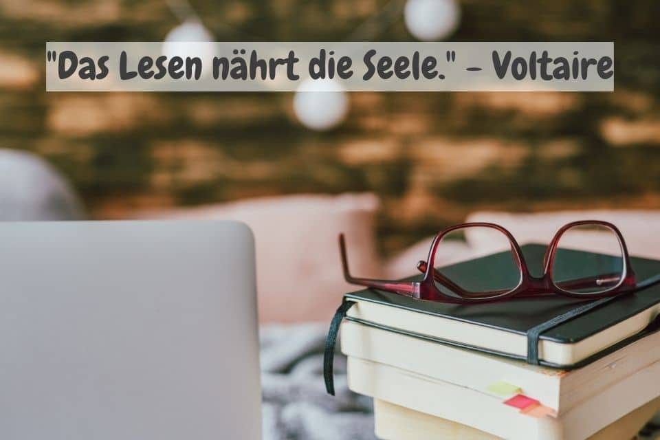 Das Bild zeigt einen Stapel Bücher mit einer roten Brille darauf, die auf einem Tisch neben einem Laptop liegen. Der Hintergrund ist unscharf und gemütlich gestaltet, mit warmen Farbtönen und Lichtern. Oben steht das Zitat: