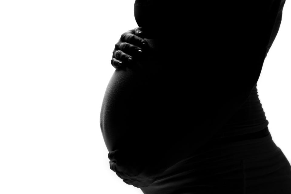 Profile of a pregnant person’s torso, with their hands cradling their belly.