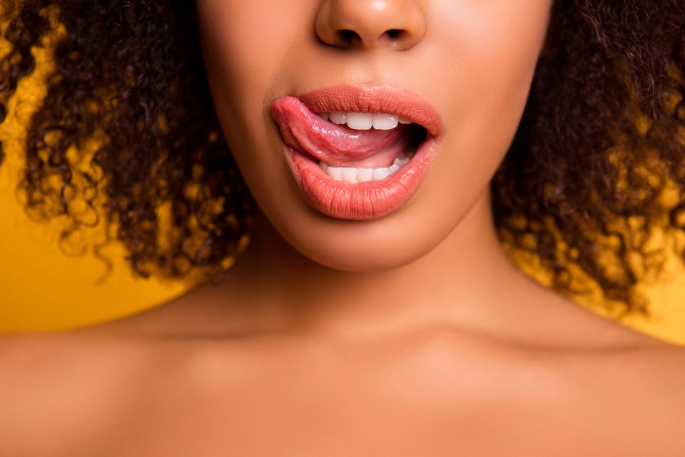 Woman’s face with tongue out, licking her top lip.