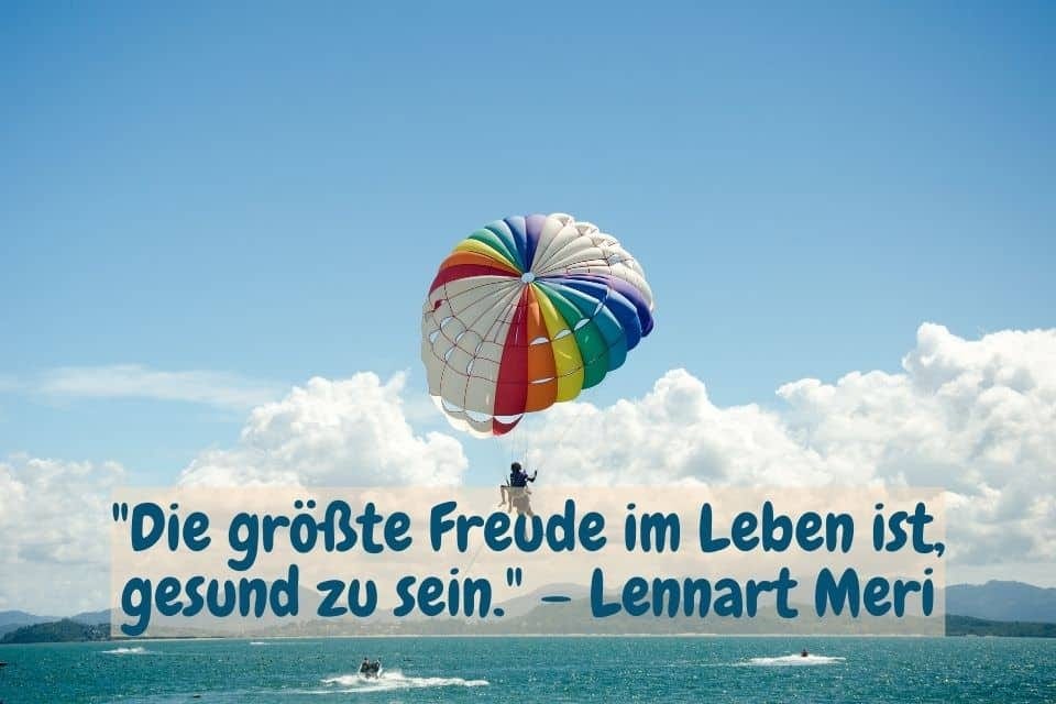 Das Bild zeigt eine Person, die mit einem farbenfrohen Fallschirm über dem Meer schwebt, unter einem klaren blauen Himmel mit einigen Wolken. Darunter steht der Text: