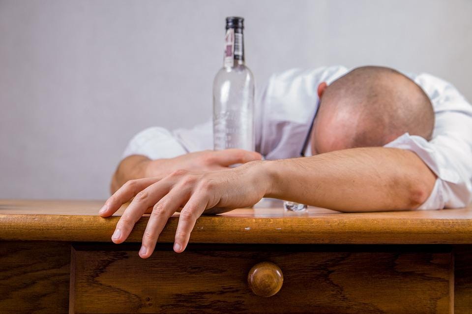 A man sleeping on a table with an empty alcohol bottle.