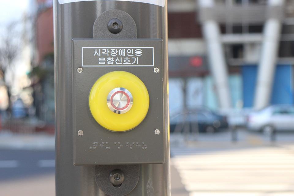Button on metal pole at crosswalk for pedestrians to request a signal to walk