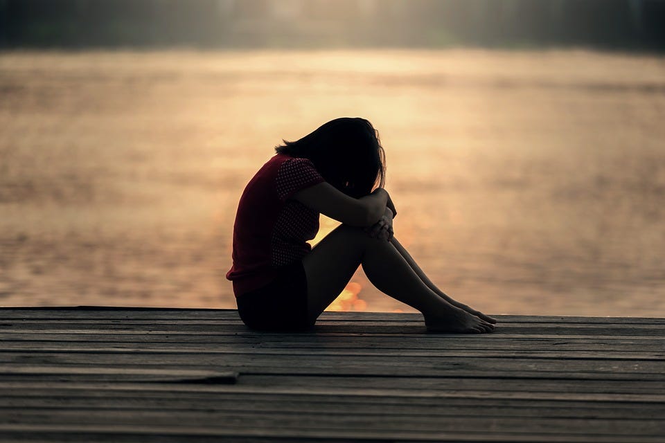 A photo of a woman sitting down while sadly contemplating by the sea