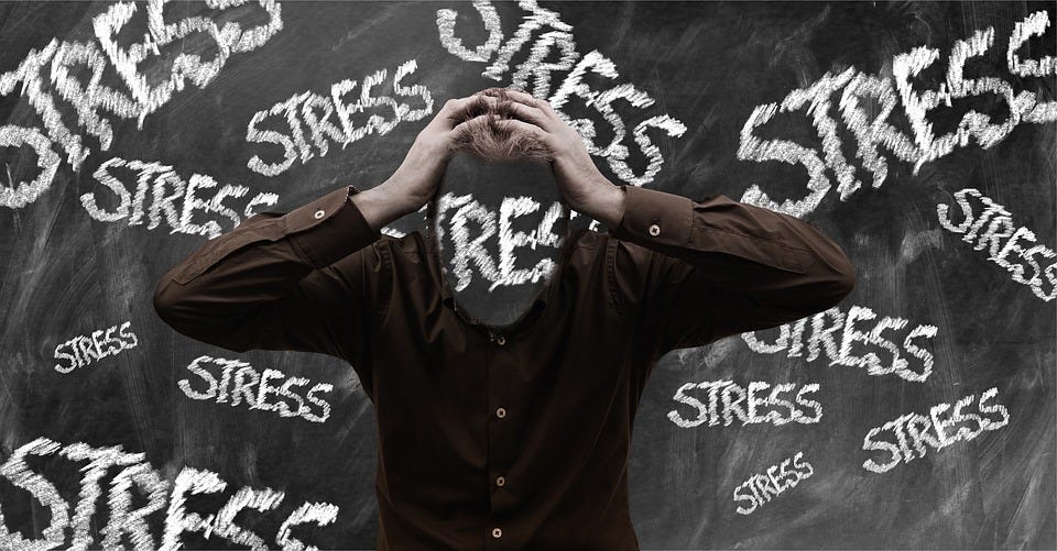 A guy standing up, holding his head, with stress written in white chalk on his face and in the background.