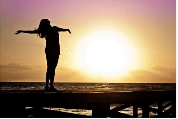 Silhouette of a woman Raising Hands Against a Sunset Light above the bridge