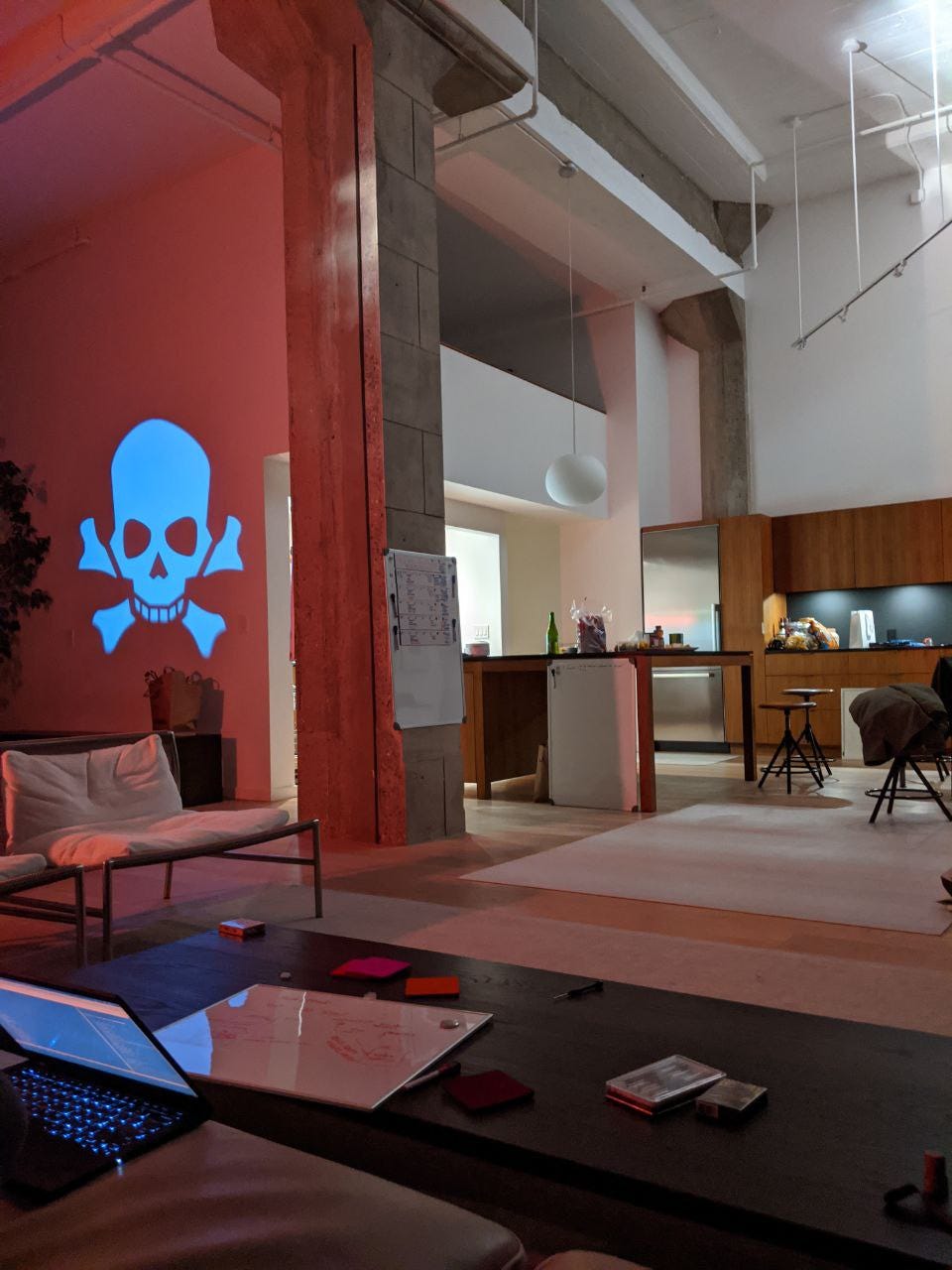 a stylish SF loft in the evening. A pirate skull and crossbones is projected onto the wall. Laptops, whiteboards, and other creative clutter is visible on every surface