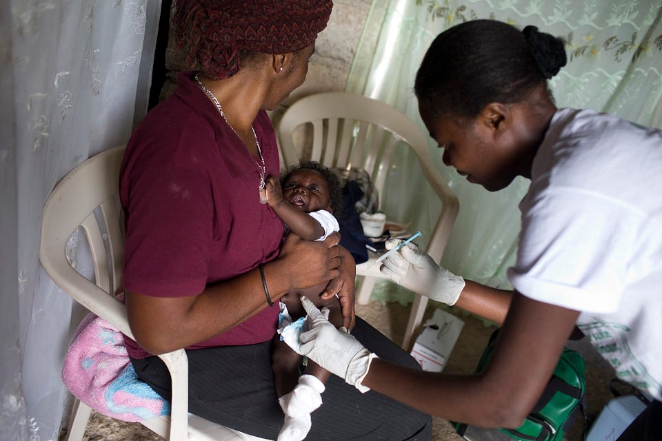 Ketcia Orilius, 37, a community health worker in Robin, Haiti, gives 3-month-old Orelus Kerlens Melus multiple vaccines. Ketcia’s house visits like this one are helping to make health services accessible in Robin, where many families can’t easily get to clinics or hospitals. / David Rochkind, USAID