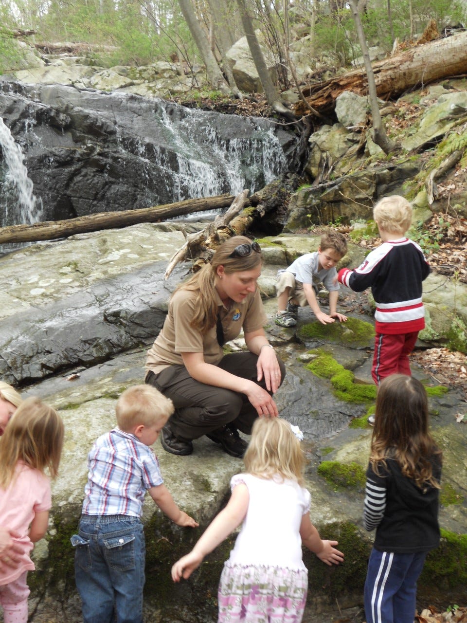 Woman in Service uniform kneels on a rock with a group of young children
