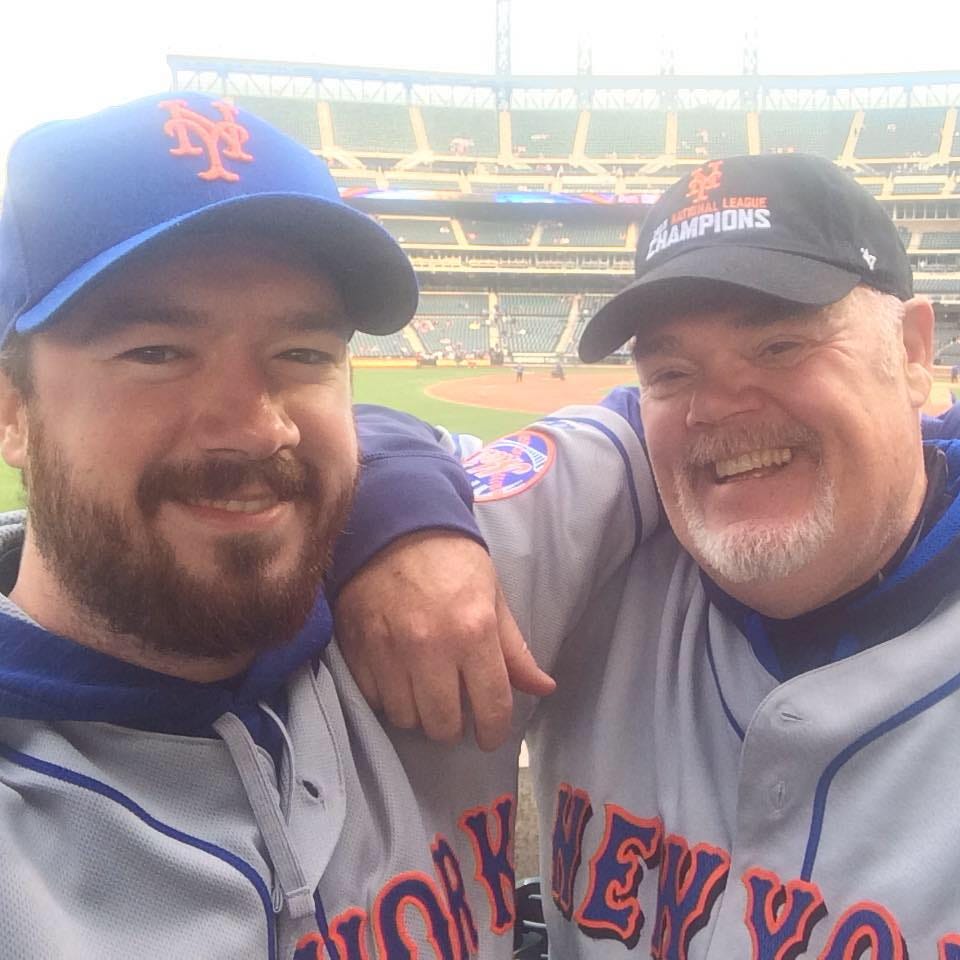 My dad and I wearing grey baseball uniforms in the stands at Citi Field in New York