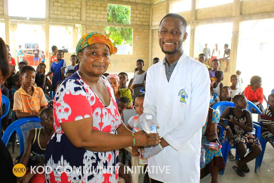 Kyeremeh, dressed in a white doctor’s coat, is giving a bottle of hand sanitizer to a woman