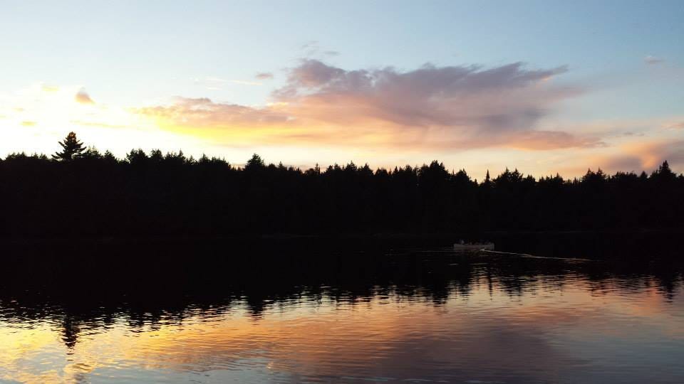 Sunrise at a lake with dark silhouettes of trees in the background and a canoe in the foreground