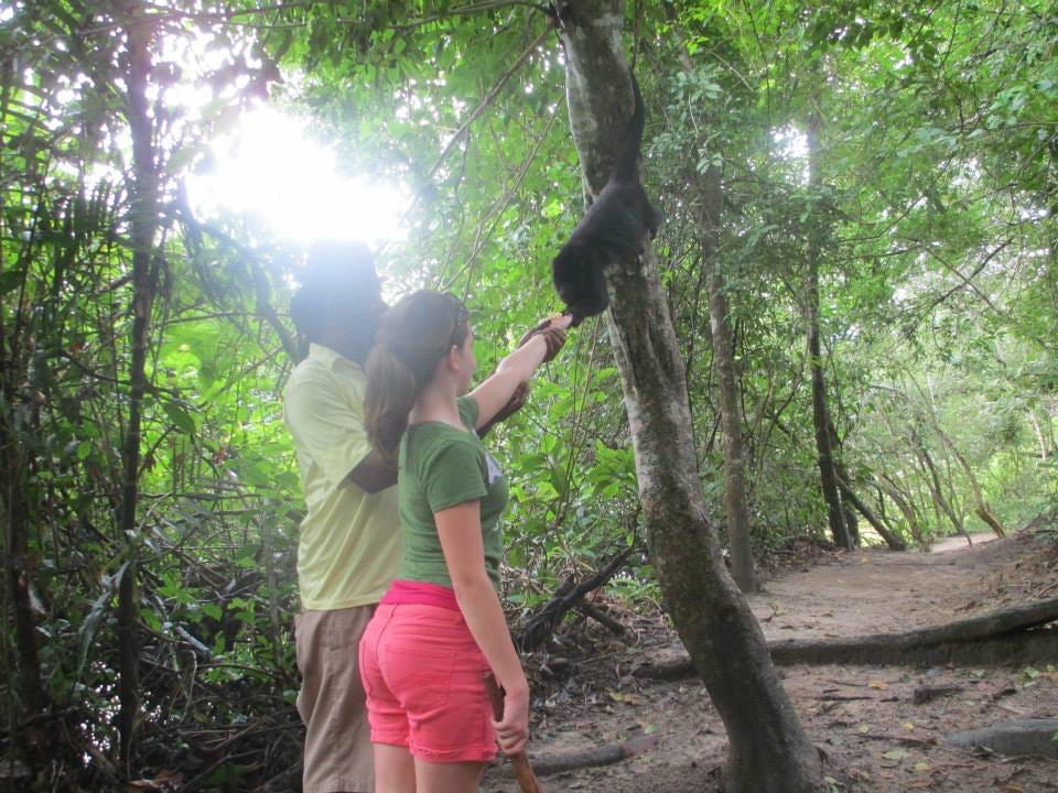 Teenage girl feeds the Howler monkey a piece of banana with the help of the guide.