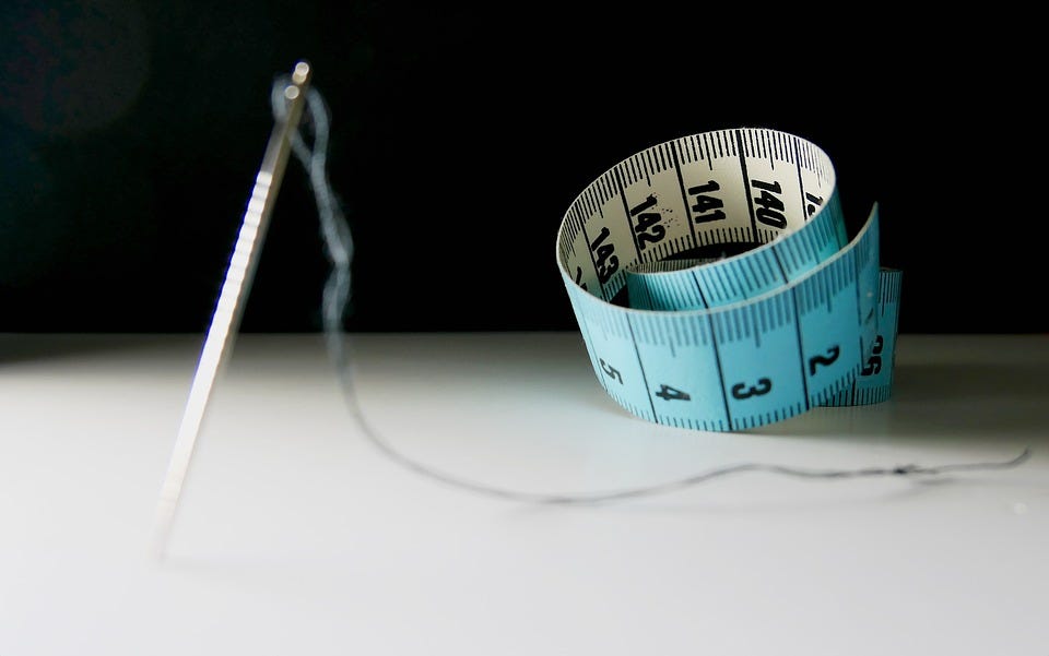 A measuring tape next to a threaded needle