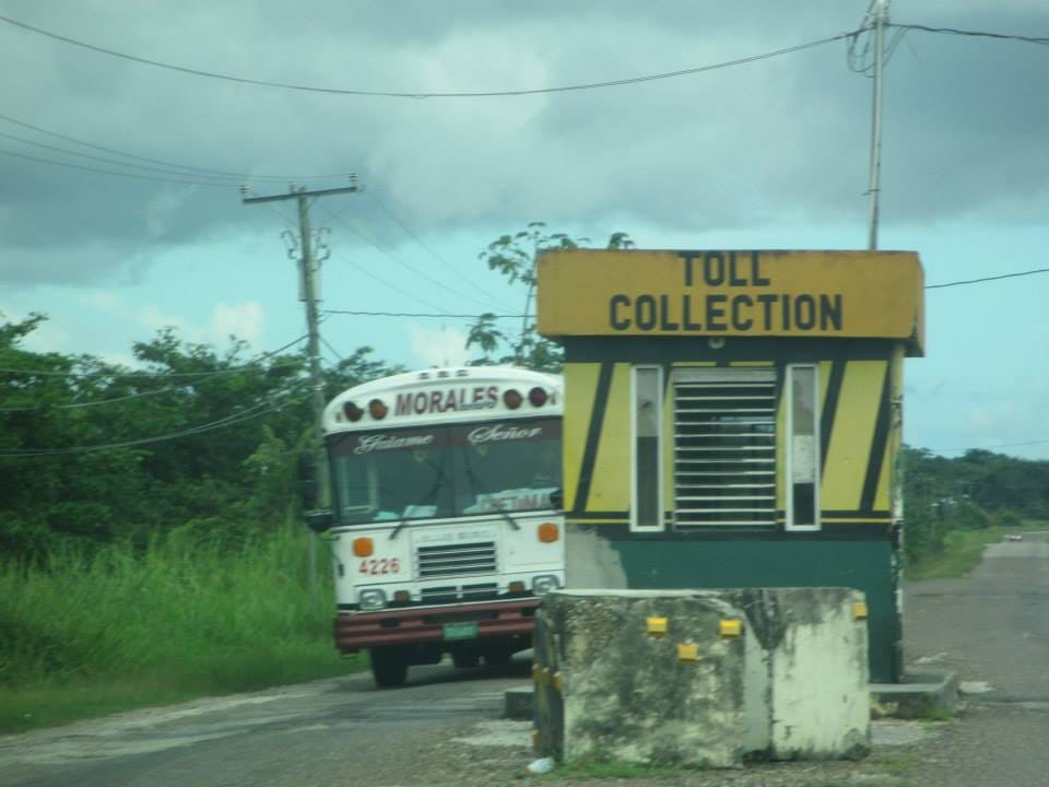 Old bus approaching a small concrete structure labeled as Toll Collection.