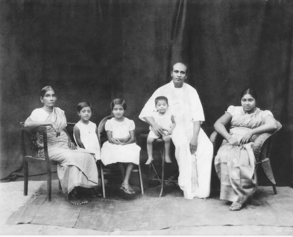 faded black-and-white picture has been restored to show an Asian family seated for a family portrait. A man in a white Sarang sits with two women in. They are accompanied by three small children.
