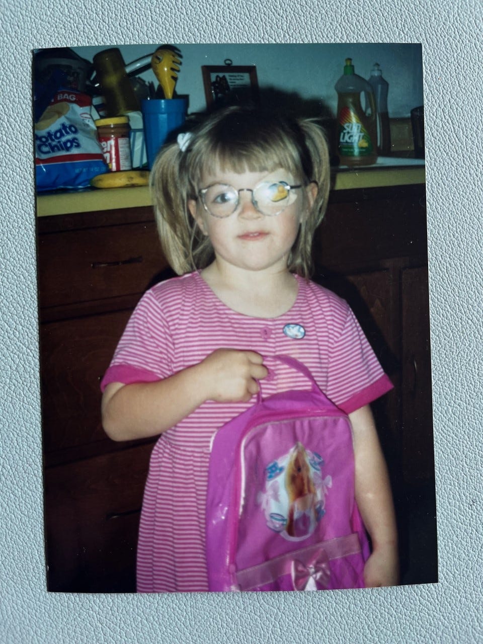 Child wearing a pink holds a backpack.