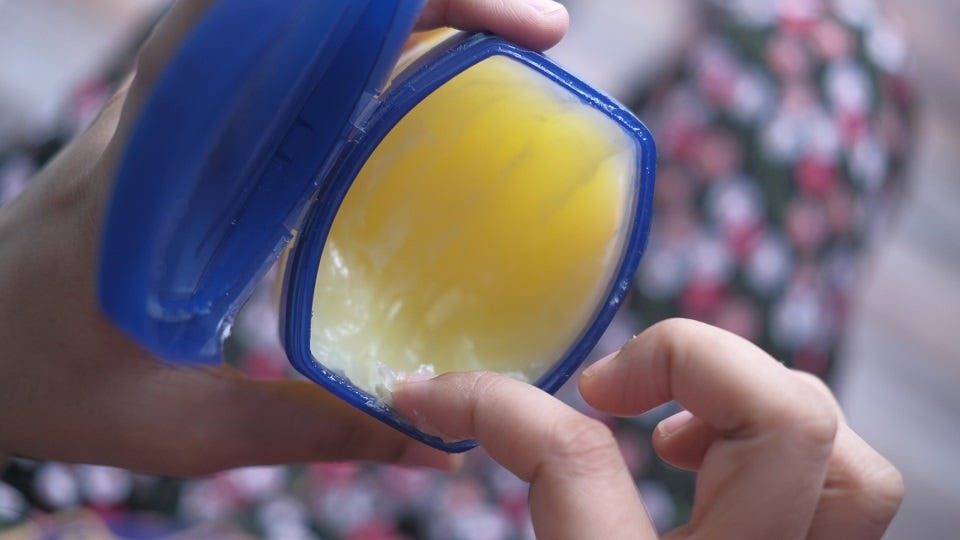 A person scooping vasline from its container