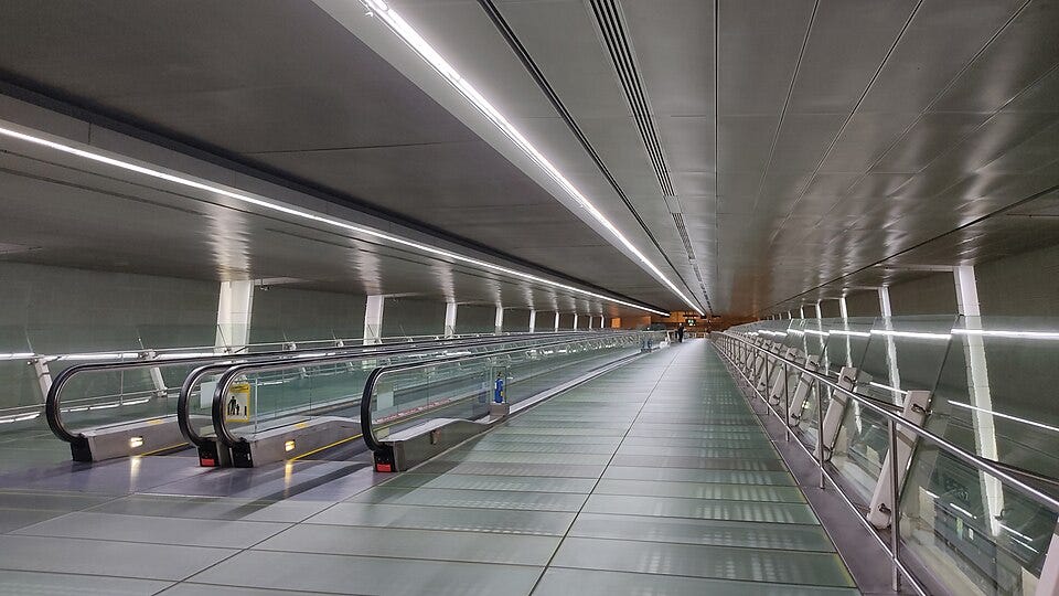 An empty, moving walkway inside a metallic tunnel.