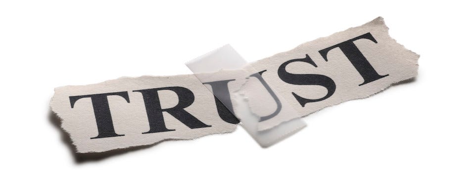 A torn piece of paper with the word “trust” written on it and a piece of tape stuck on it