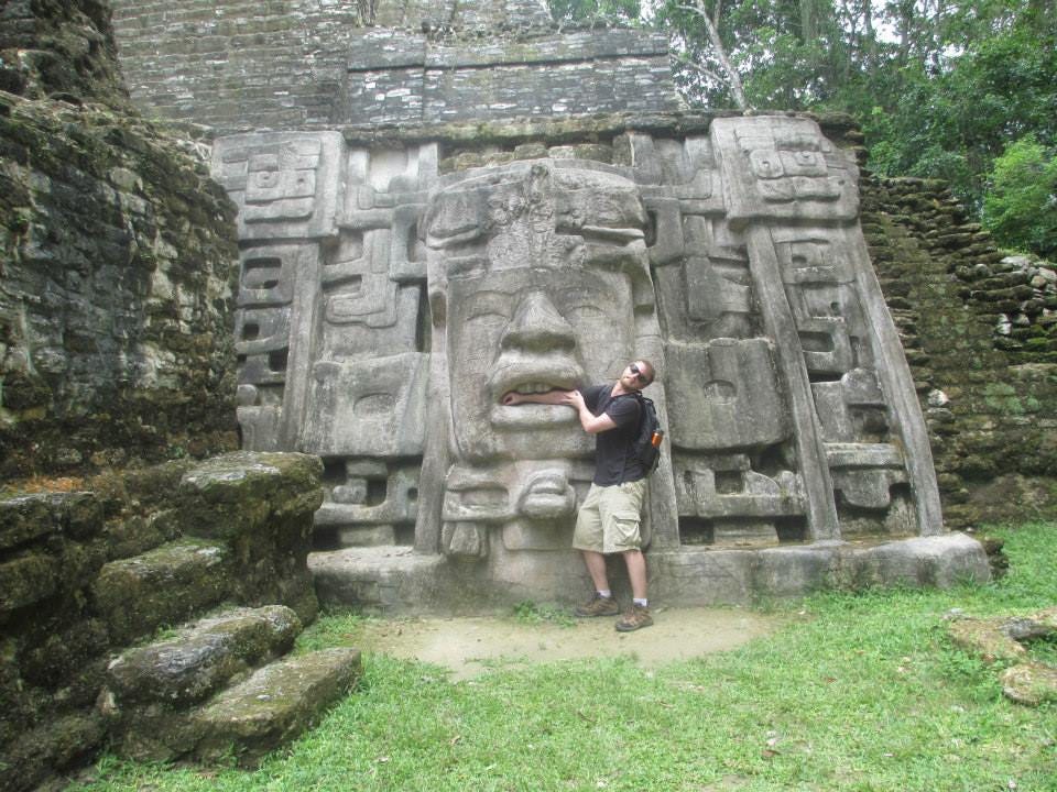 Author’s son poses in a silly position with his arm between the lips of a face in the Mayan temple and an exaggerated facial expression as though his arm is being eaten.