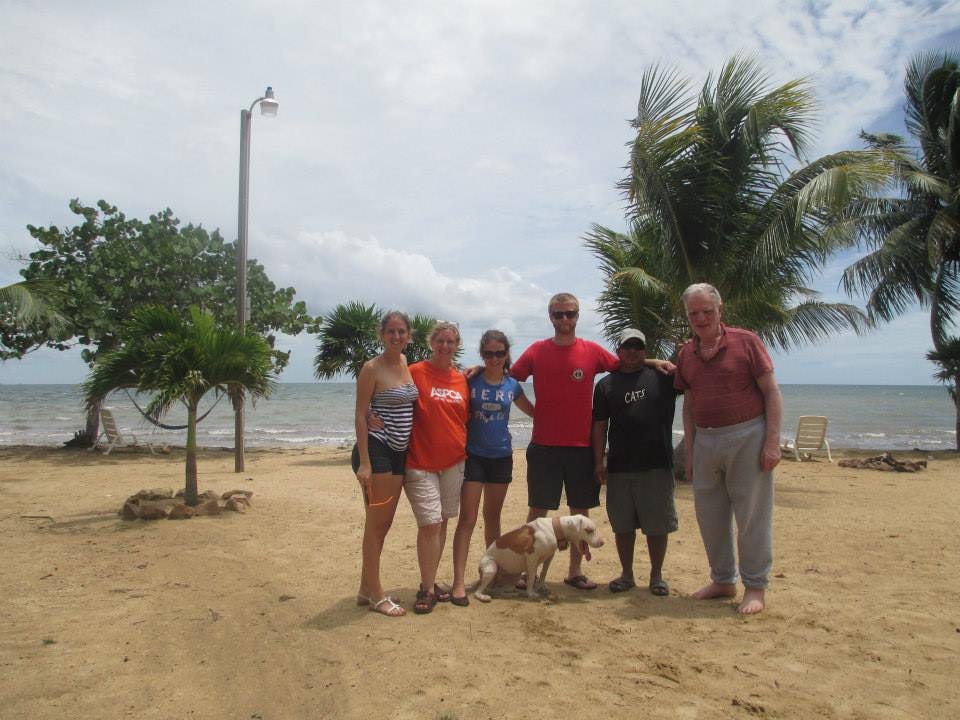 Author with her family, the property manager (a black man), and the property owner (middle-aged white man) stand in a friendly pose on the sandy beach with the property owner’s dog sitting at the feet in the middle.