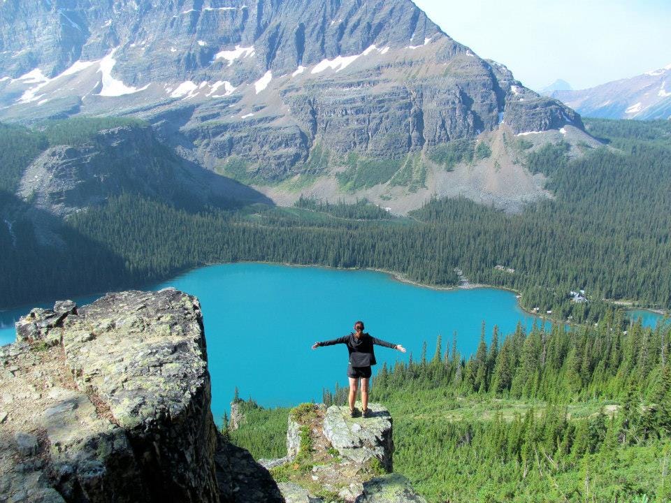 Jenna stands on a jutting rock overlooking Lake O’Hara in Yoho National Park. Her arms are outstretched as she takes it in.