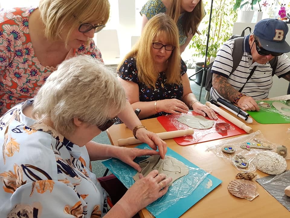 A man and two women who are deafblind use clay to create art pieces supported by two female helpers