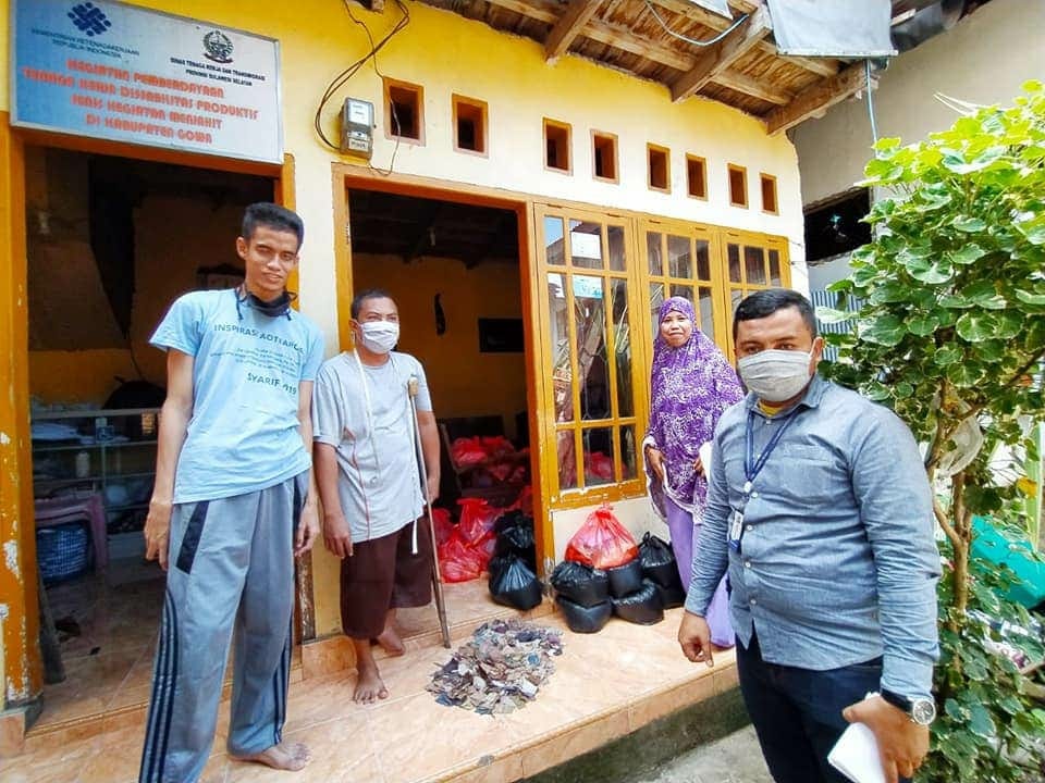 4 people stand in front of a house-like structure. Two people stand on either side of the photo, and bags of food deliveries