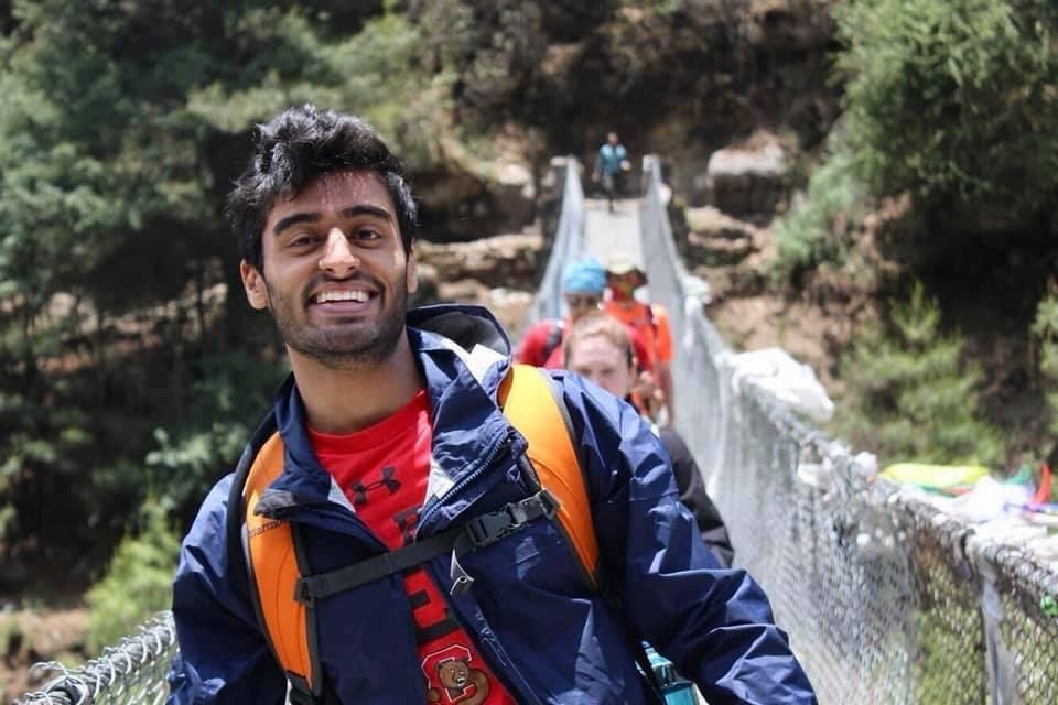 Zubin Patel hiking across a rope bridge with other hikers.