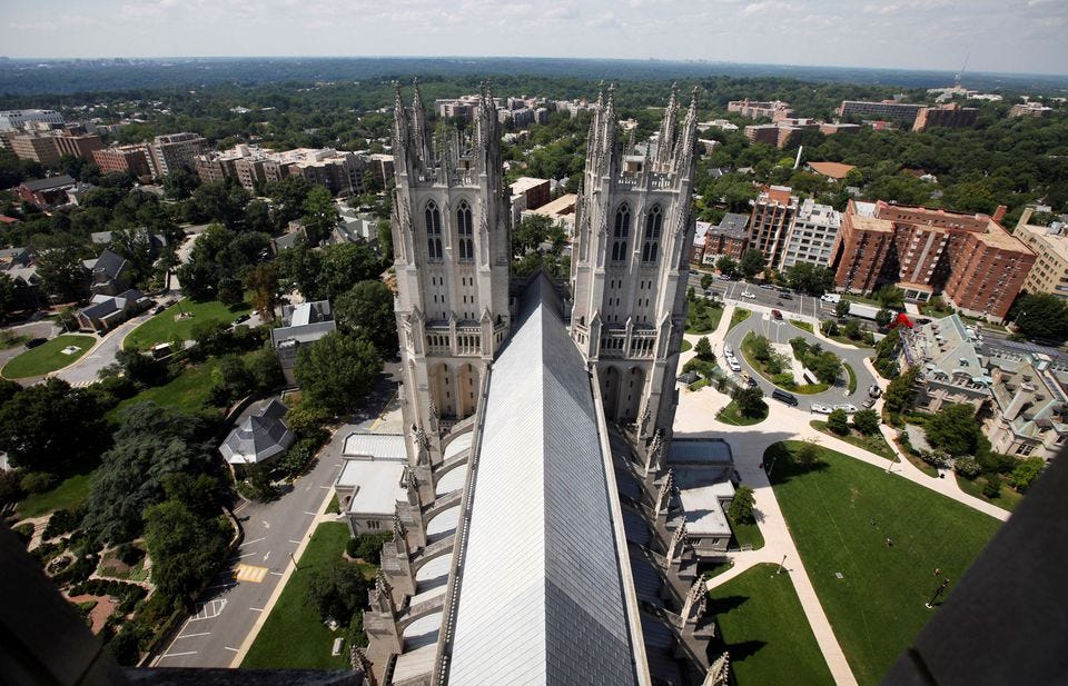 Looking down on the roof of the cathedral, and at the backs of the two front towers, the cathedral grounds far below fill most of the picture. Apartment blocks and other modern buildings appear at the top of the picture, just below the horizon.