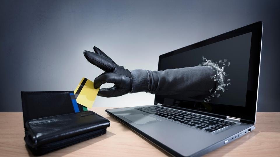 Fully clothed in black mysterious hand breaking through laptop screen to steal gold credit card from leather wallet, stealing online thieves scammers digital theft