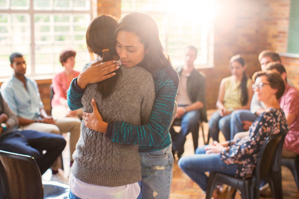 Two women hugging in group therapy session.