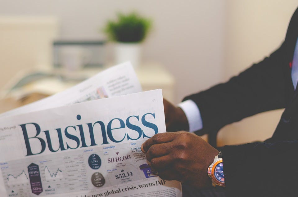 A newspaper called ‘Business’ is held in the hands of a person with a shiny watch and dark suit.