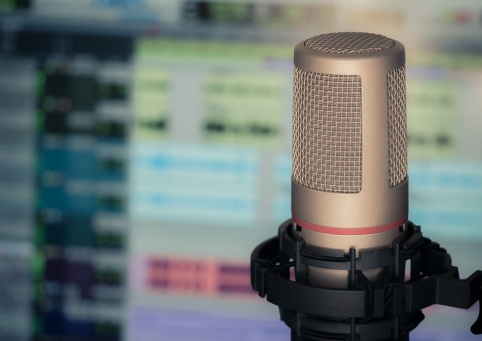 A photo of a microphone in front of a blurry background of an audio recording software screen.