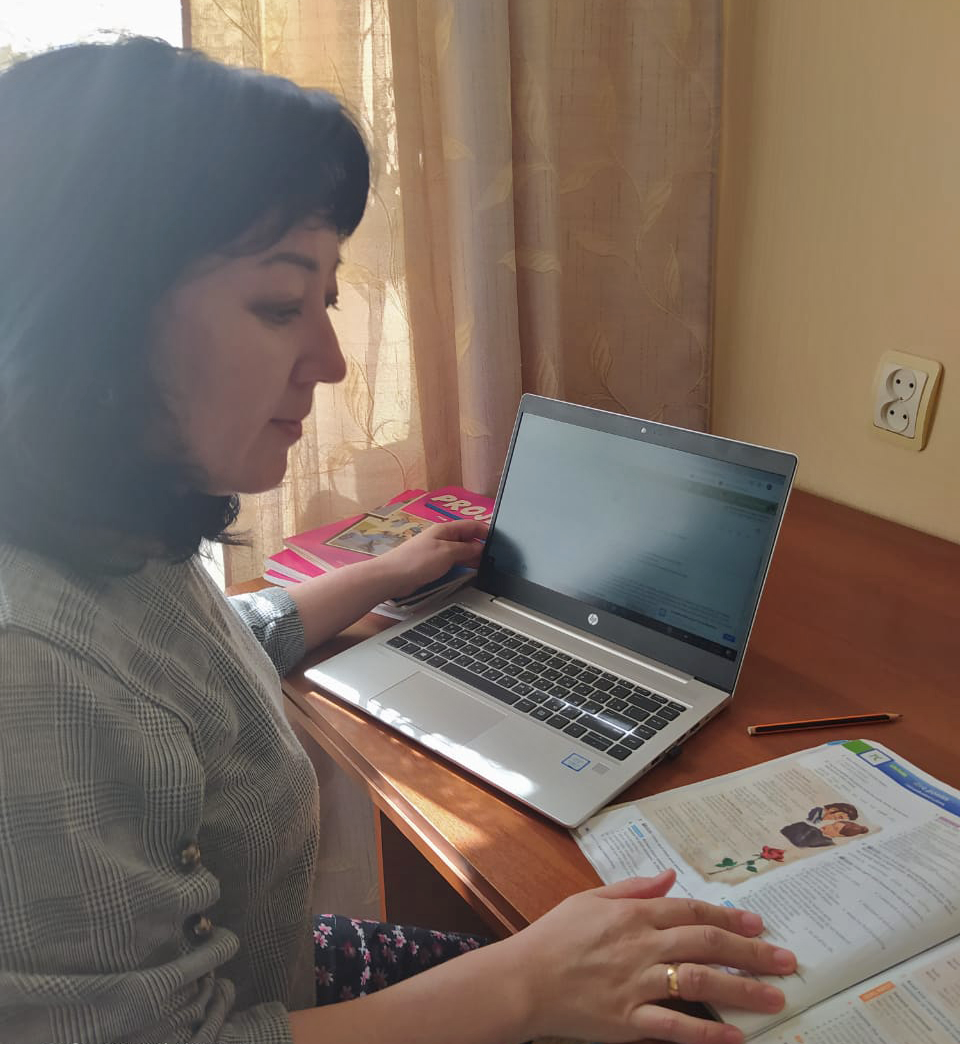 A woman sits at a desk in front of a laptop and looks at an instructional booklet.