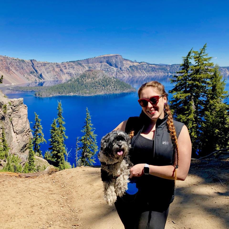 Deanna with her dog on a cliff overlooking a lake and mountains.