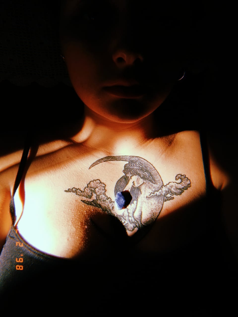 picture of a tattooed female chest, with a drawn moon and a little blue stone above the tattoo.