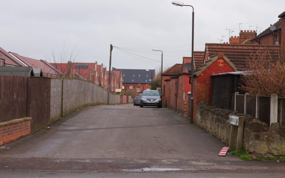 An empty residential street with red brick houses under a grey sky