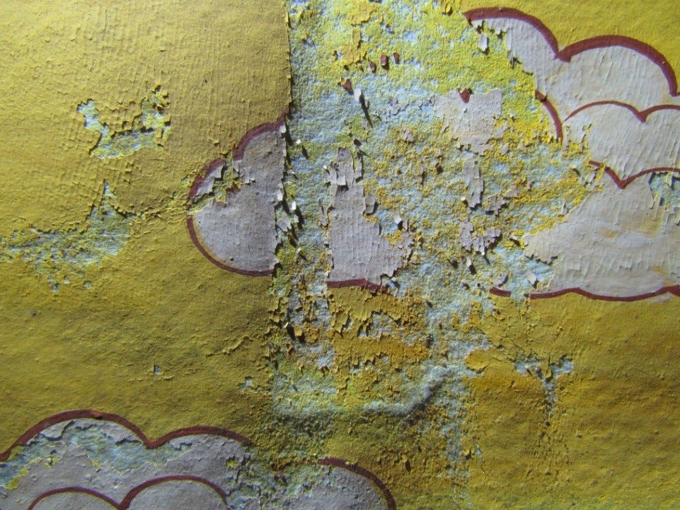 A close up of a painting with a yellow background and white clouds. The paint layer is flaking off and powdering in many areas, with some losses.