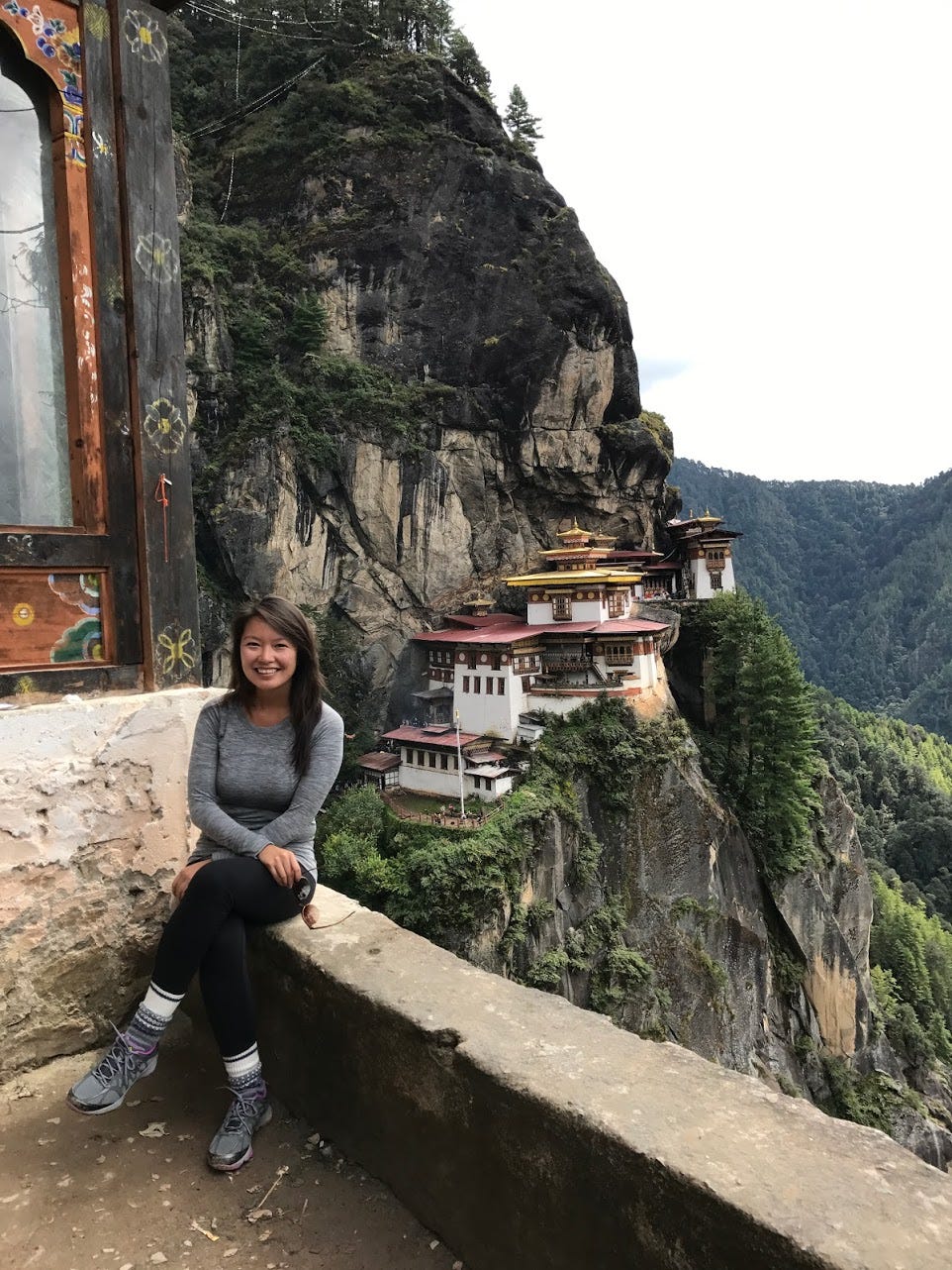 The Author sits next to a cliff that overlooks the Tiger’s Nest in Bhutan.