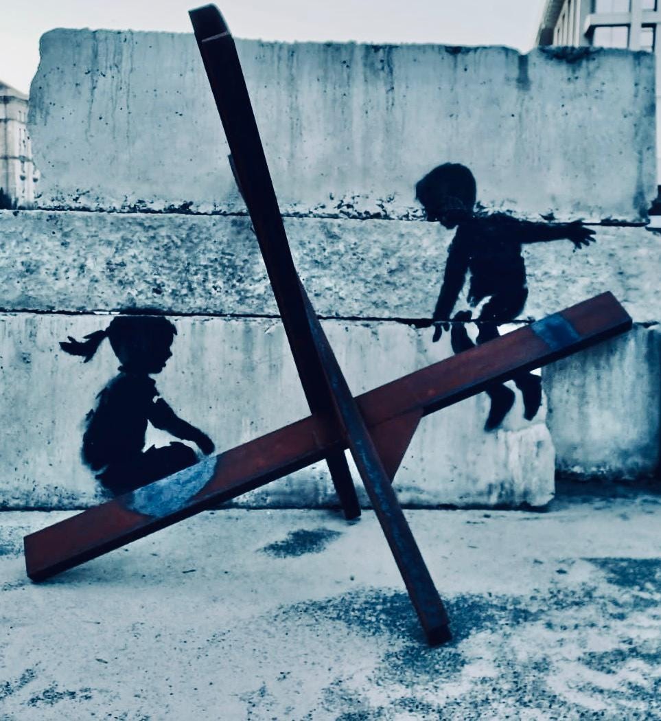 Street art in Kyiv, Ukraine, by Banksy. A tank trap sits against concrete blocks. A Banksy stencil gives the impression of a little girl and a little boy using the tank trap as a see-saw. All photos in the The Machine Race series are in black and white representing binary computer code and binary views that often fill the AI debate.