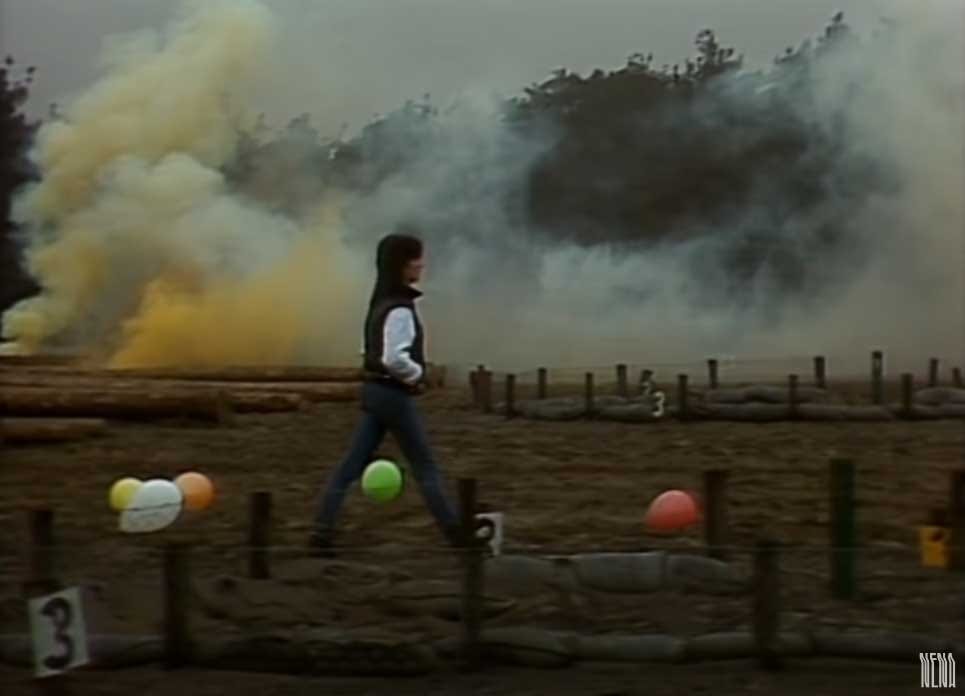 Image of Nena walking through a field with balloons and smoke in the background, from the music video for 99 Red Balloons.