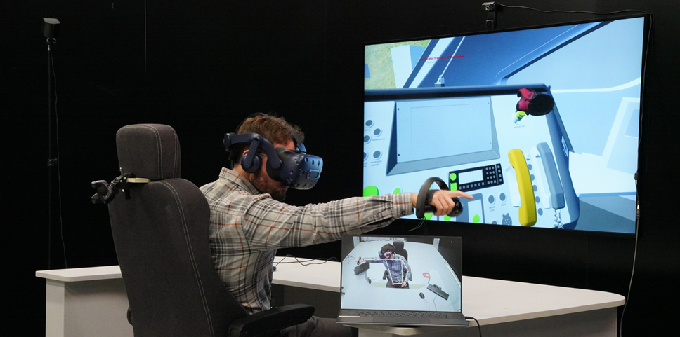 Photograph showing a person in a Train Cab mock up wearing a VR headset — The image that they are looking it is shown on a TV screen