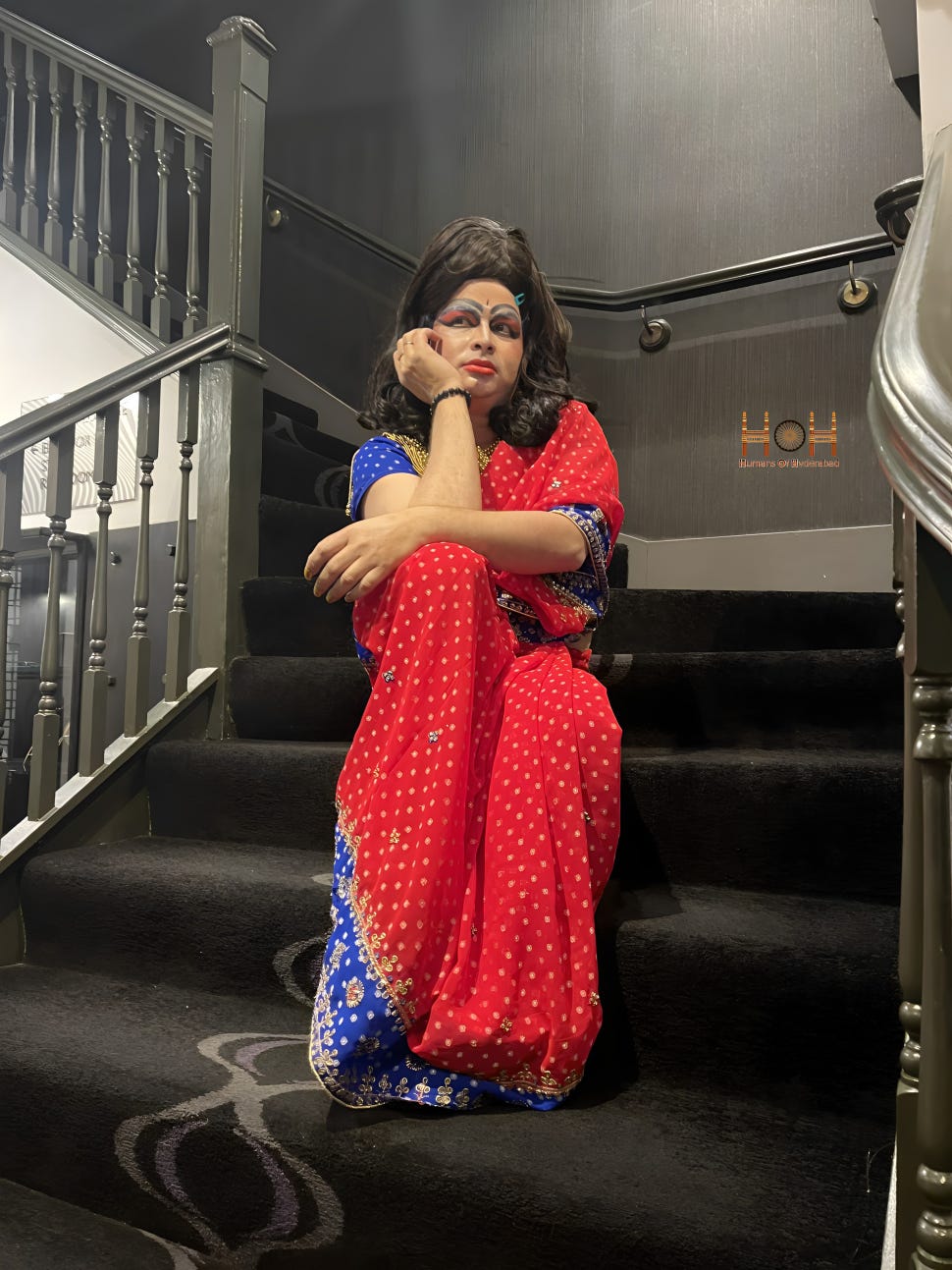 An adult poses on the stairs while wearing traditional Indian drag outfit.