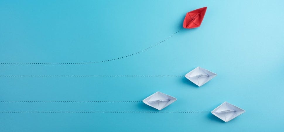 Three white paper boats on a straight line path, one red paper boat on its own unique path