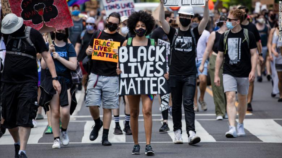A woman marches to the White House along with others holding a Black Lives Matter sign.