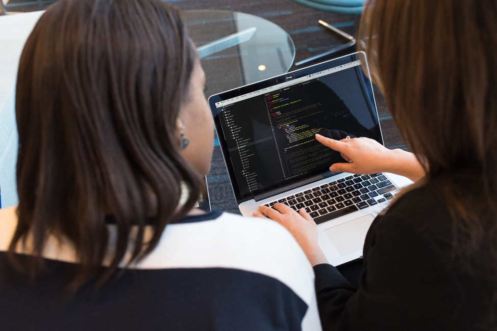 Stock image of two women looking at code on a laptop and pointing.