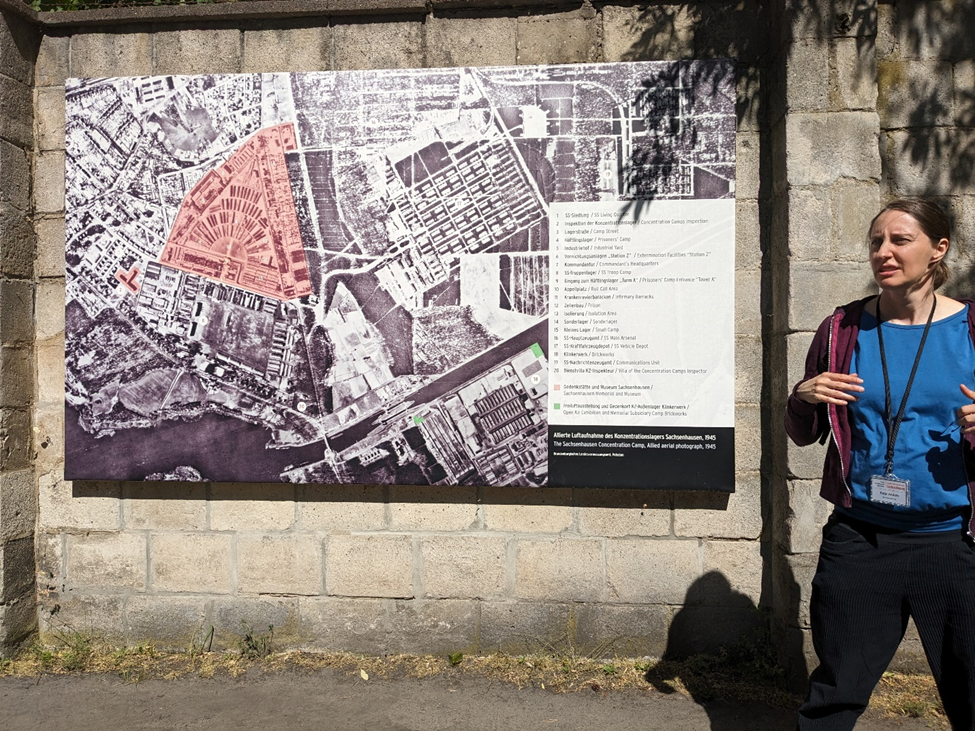 A woman in front of an aerial photograph of a concentration camp